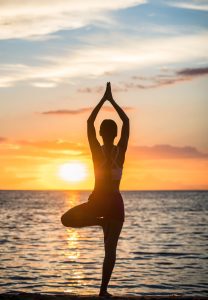 Fit woman practicing the yoga tree pose for a toned body on an idyllic beach at sunset
